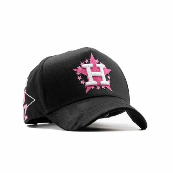 Gorra “Clave Ali” - Vista Diagonal con Bordado H y Estrellas Vista frontal en ángulo mostrando la H blanca sobre estrella rosa, con detalles adicionales en visera y costado.