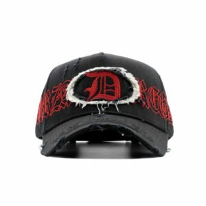 Gorra negra con parche rasgado al frente, letra D roja bordada y texto REGIDA, estilo urbano de la colección Dandy x Fuerza Regida.