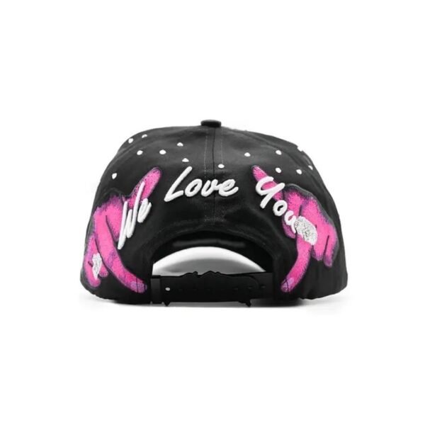Parte trasera de la gorra con frase “We Love You” y diseño artístico Parte posterior de la gorra Dandy Hats con frase bordada “We Love You” y manos rosas
