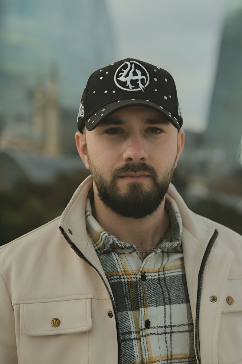 Hombre con barba vistiendo una gorra negra Dandy Hats x Lost Hills — LH Chrome decorada con pedrería y logotipo cromado, posando en un entorno urbano moderno.