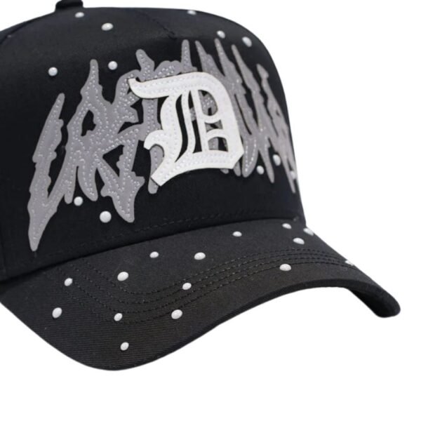 Primer plano del logo bordado “D” en gorra Lost Dandy Detalle del bordado central blanco y gris sobre la visera de la gorra negra